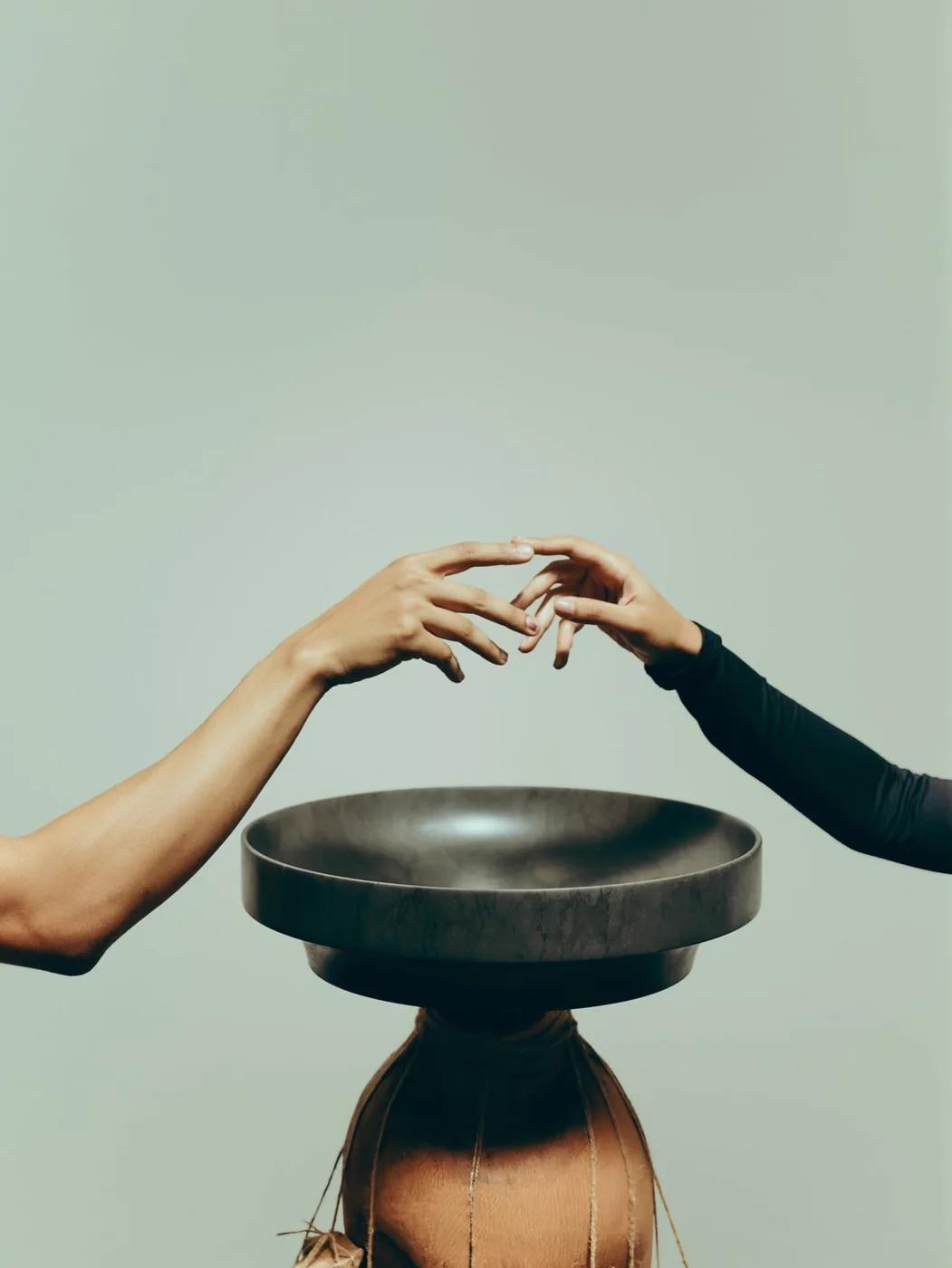 Hands reaching towards a dark marble Römer basin balanced on a carved wooden base